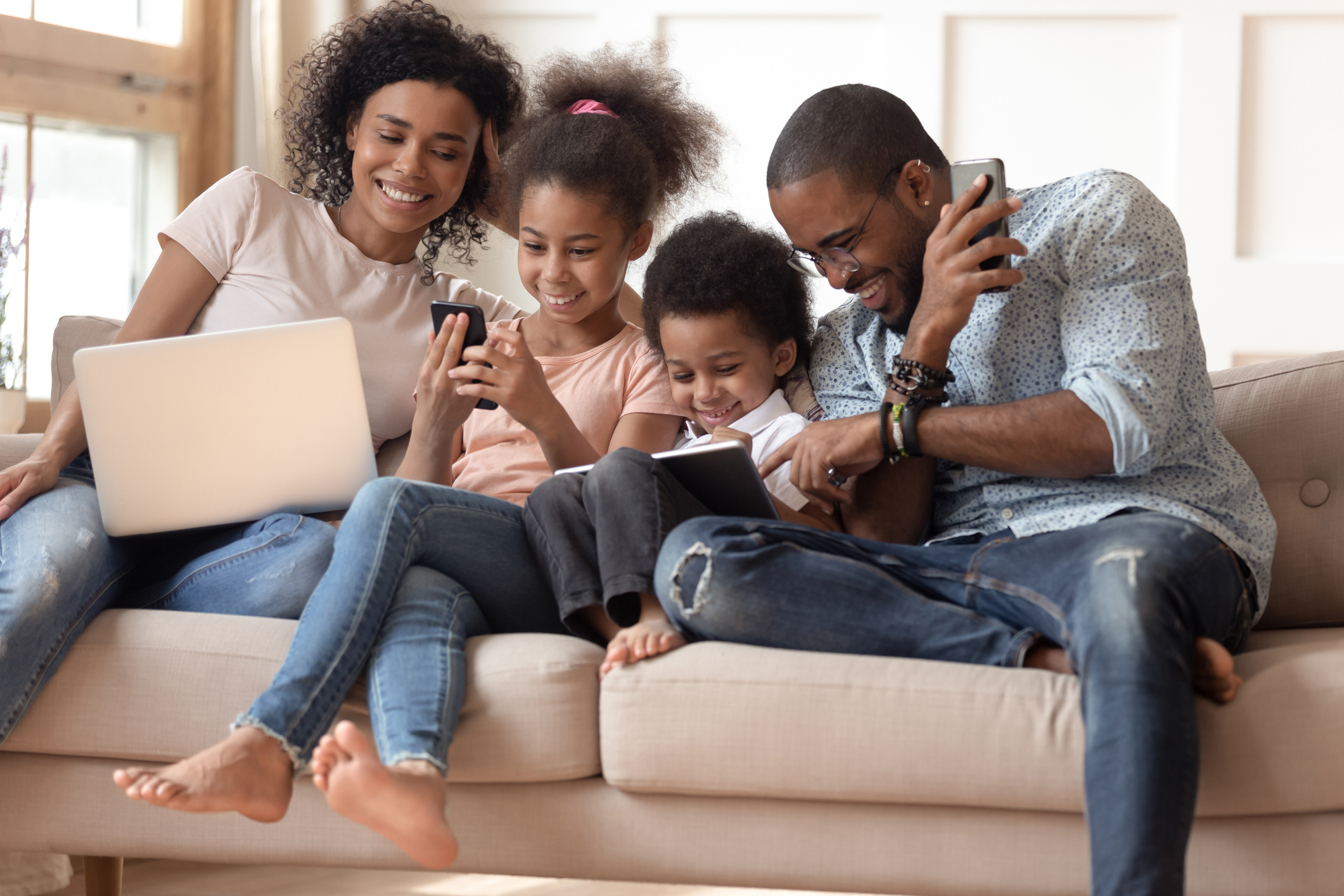 Family sitting on couch playing together with laptop, phone, and tablet