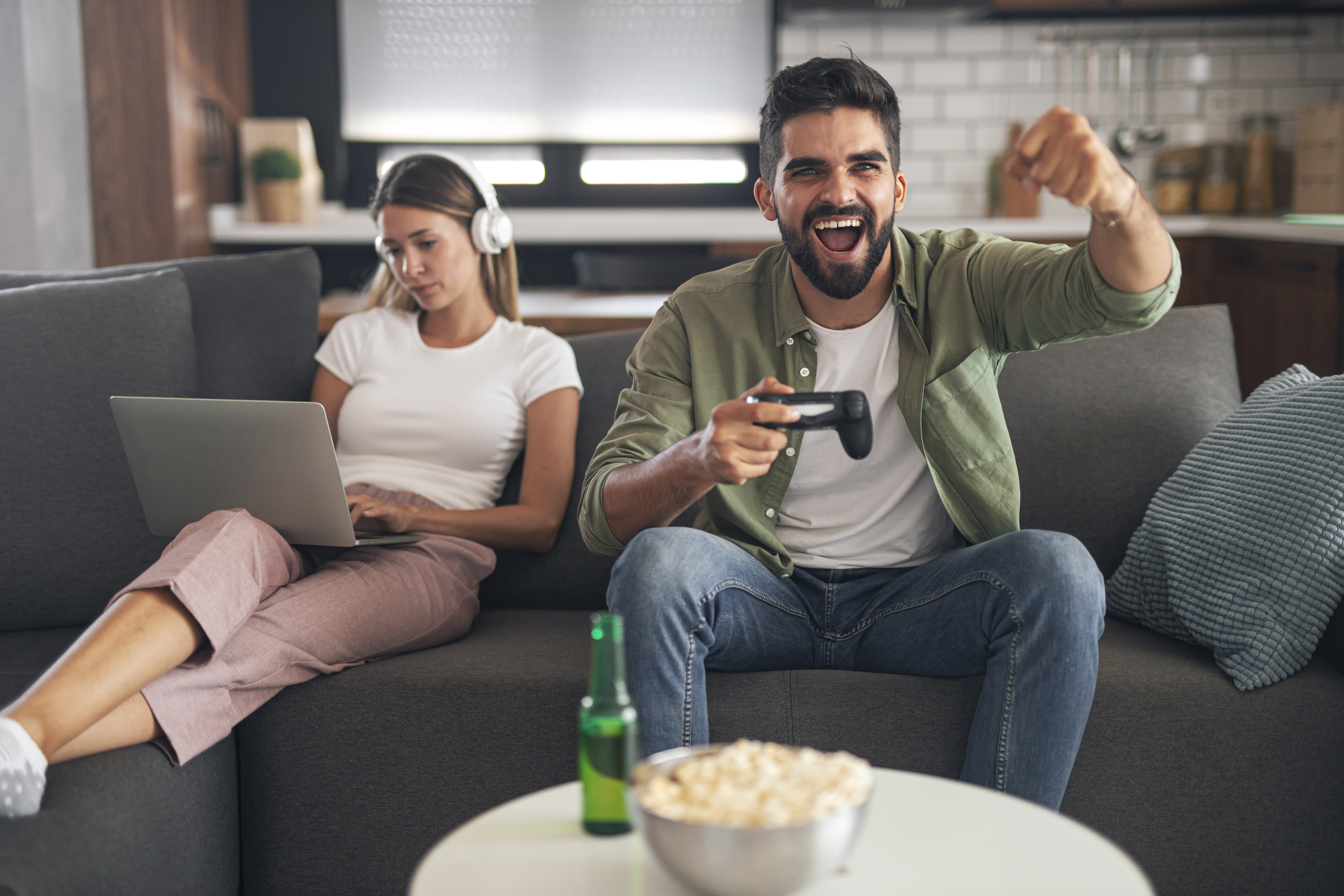 Overjoyed man holding joystick, celebrating victory in video game. Bored women working on laptop in the background