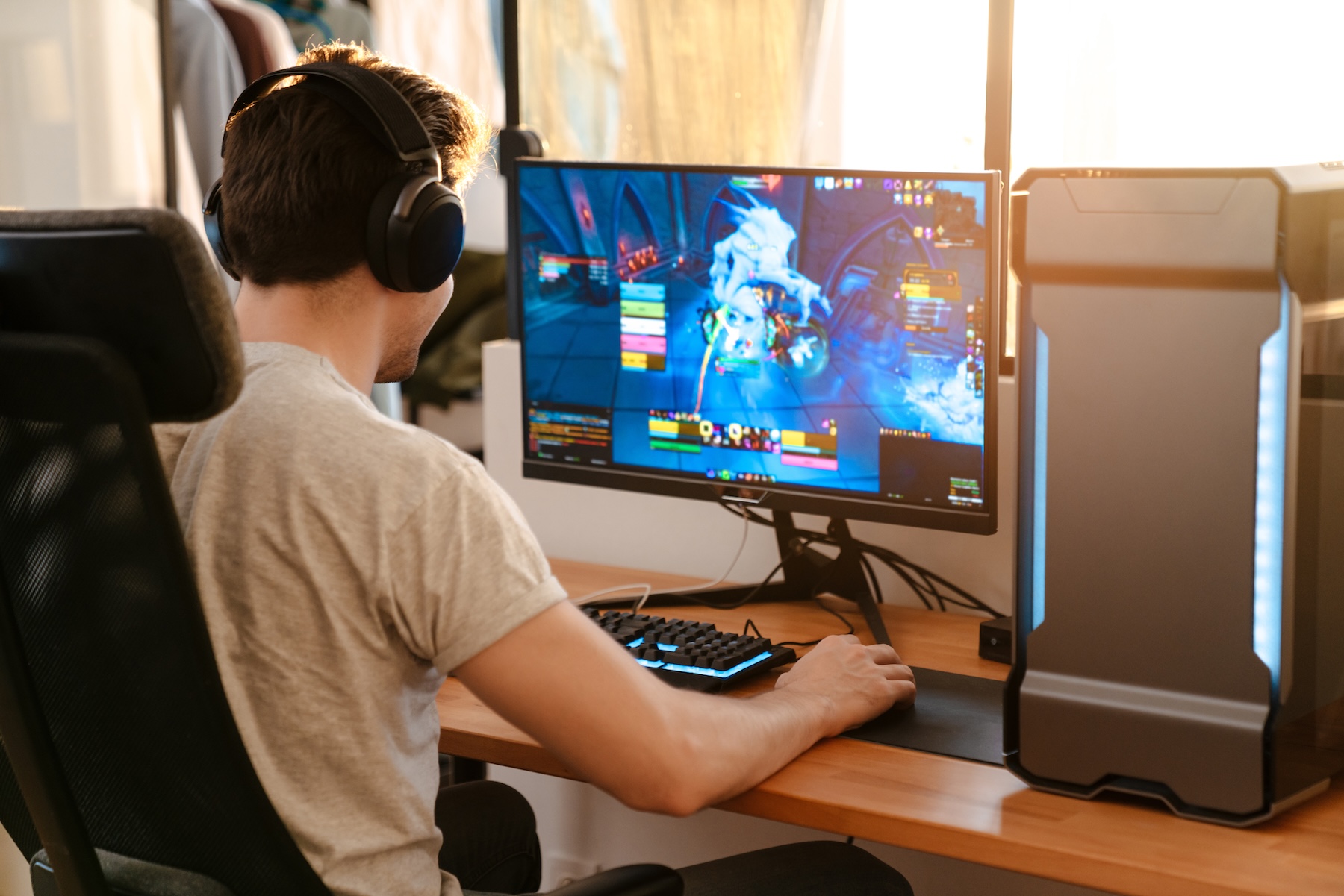 White male gamer playing on PC setup with sun coming through windows