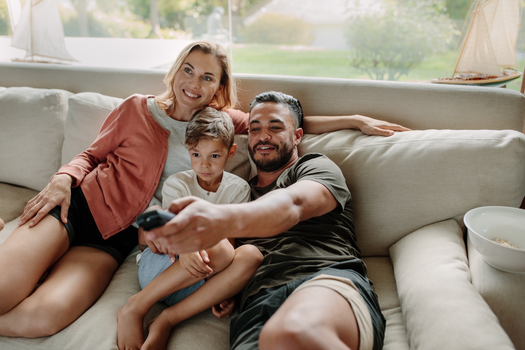 Family of three sitting on a sofa and watching TV together at home.