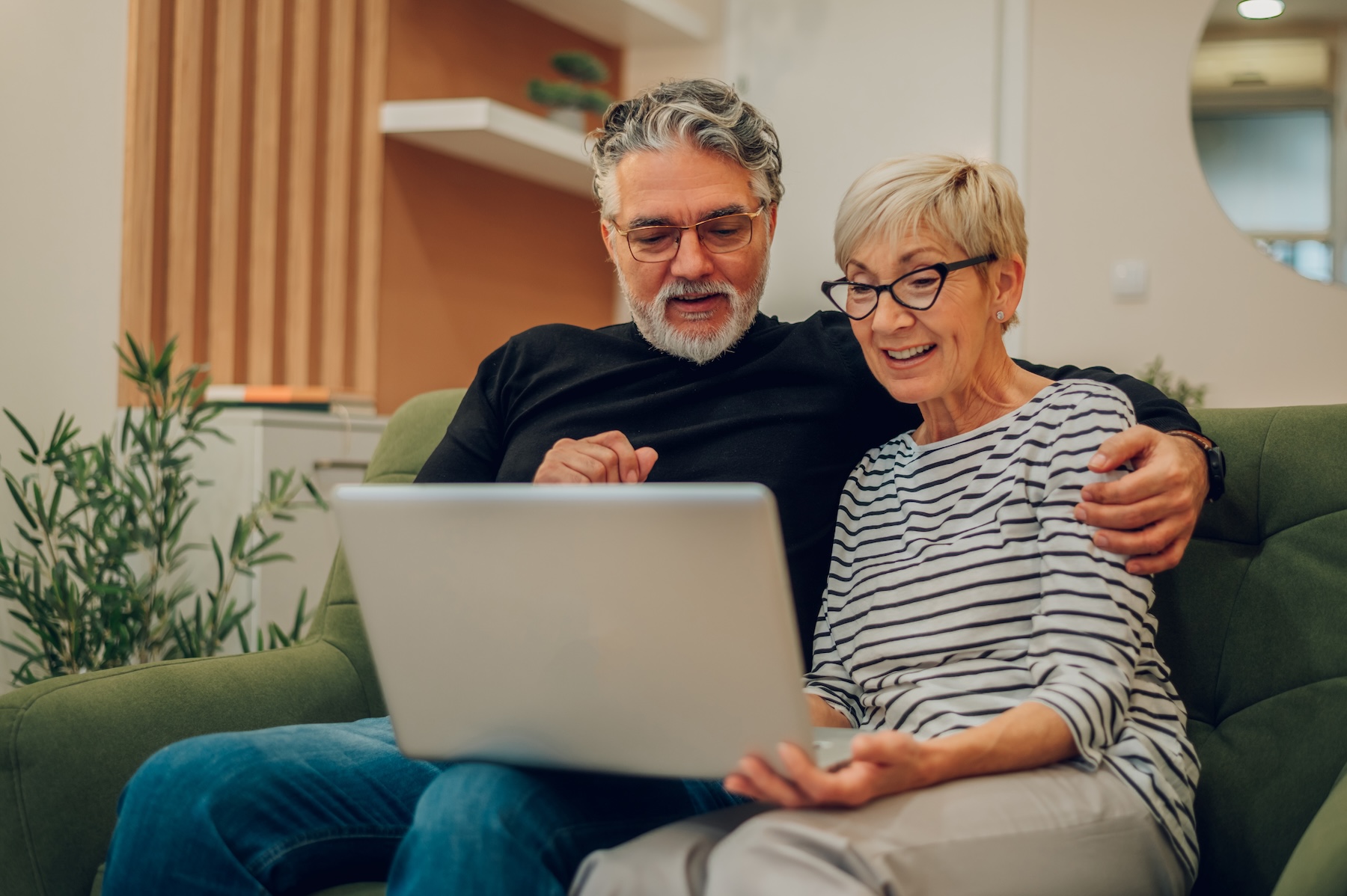 Senior married couple embracing on couch, using laptop together