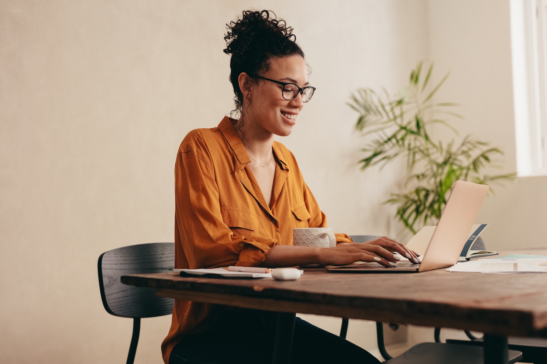 Woman working on laptop computer at home, sitting at table with a coffee cup